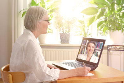 woman in her sunny living room in front of a laptop making notes