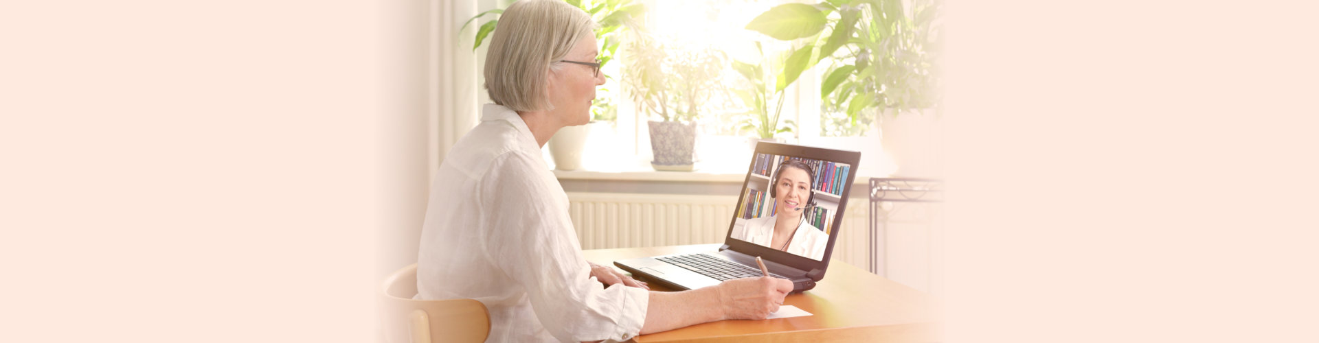 woman in her sunny living room in front of a laptop making notes